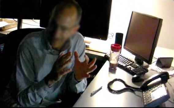 A radiologist gesturing animatedly while sitting in his reading room between three monitors and a landline