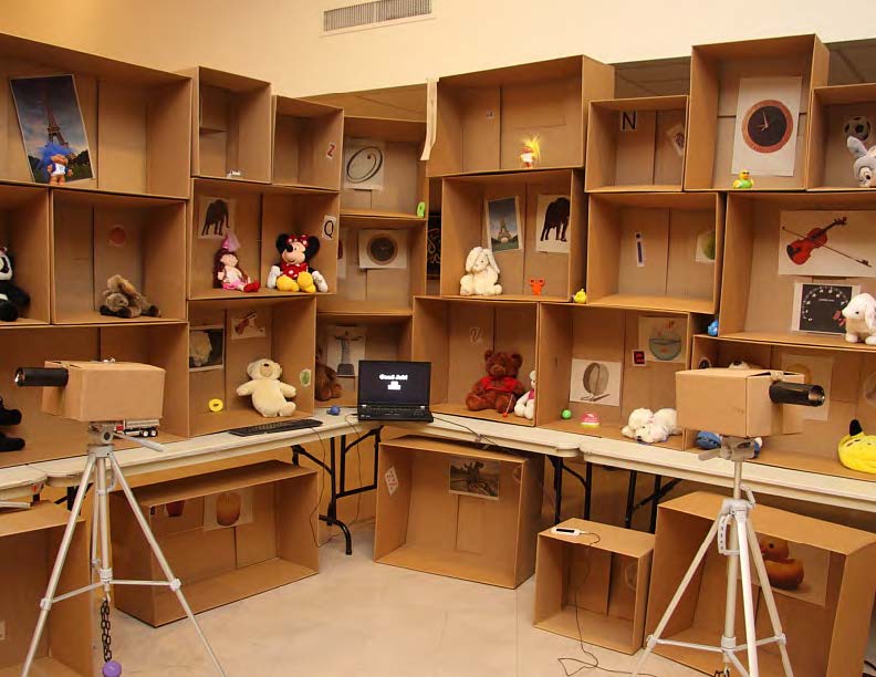 A wall of stacked boxes with their openings facing us, each containing a variety of differently sized and colored items such as toys and printed photographs